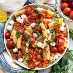 gluten free pasta salad in a bowl with pasta, mozzarella balls, tomtatoes and basil
