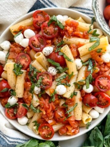 gluten free pasta salad in a bowl with pasta, mozzarella balls, tomtatoes and basil