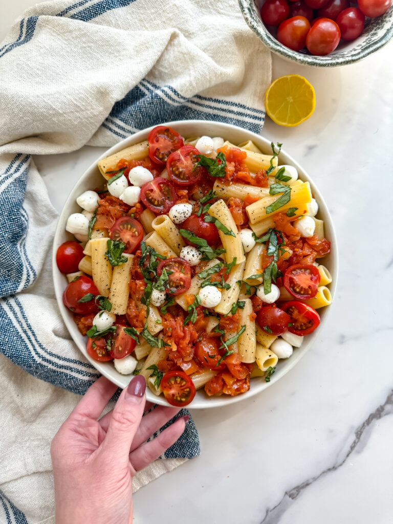 gluten free pasta salad in a bowl with pasta, mozzarella balls, tomtatoes and basil