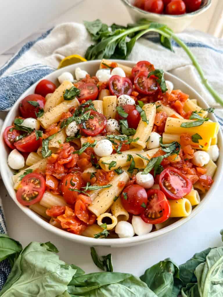 gluten free pasta salad in a bowl with pasta, mozzarella balls, tomtatoes and basil