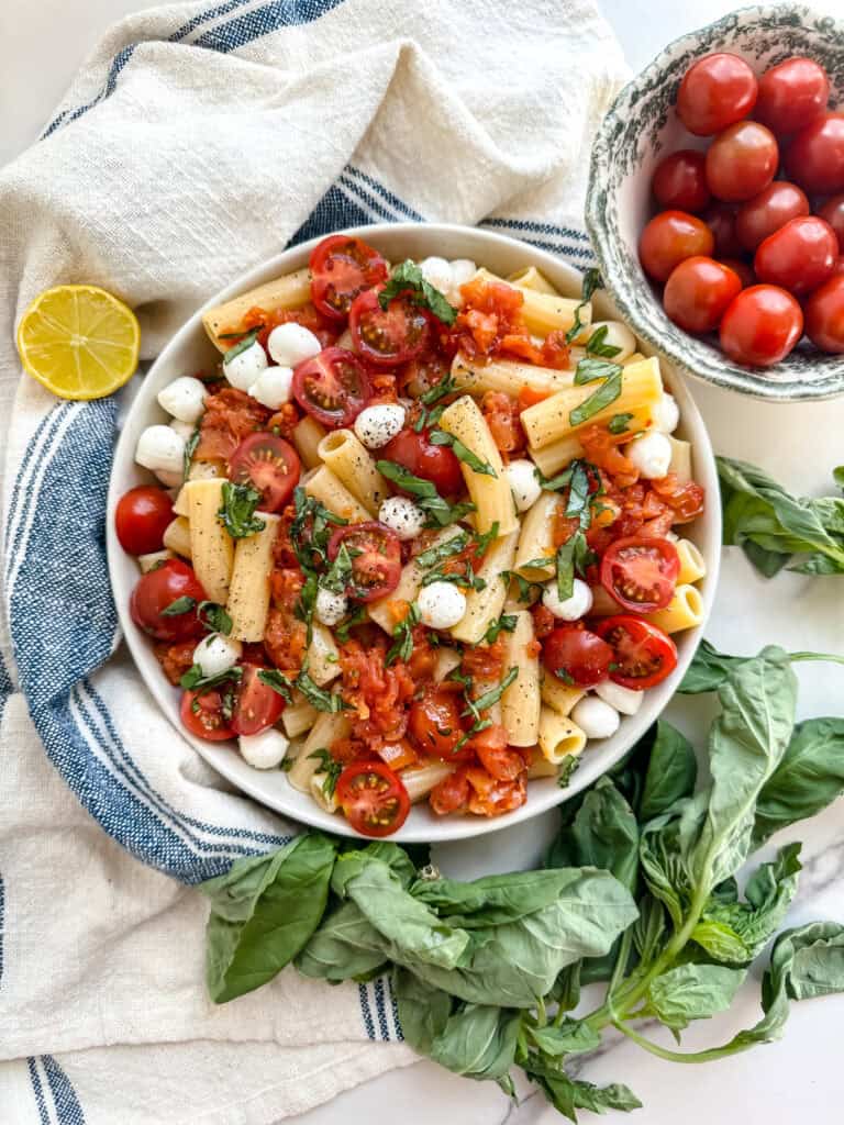 gluten free pasta salad in a bowl with pasta, mozzarella balls, tomtatoes and basil
